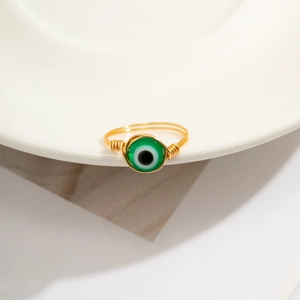 Detail of handmade gold wire-wrapped ring featuring a green Evil Eye bead on a tray