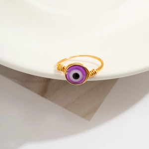 Macro detail of handmade gold wire-wrapped ring with a purple evil eye bead on white ceramic