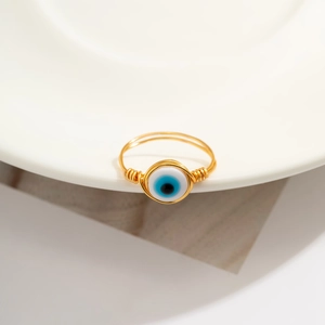Macro detail of handmade gold wire-wrapped ring with a blue evil eye bead on white tray