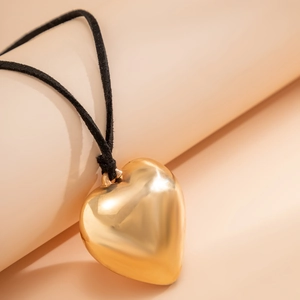 Macro shot of polished gold heart pendant with black cord on minimalist display