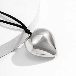 Close-up of a large polished silver heart pendant on a black adjustable cord necklace