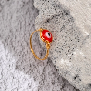 Handmade gold wire-wrapped ring with a red evil eye bead on a natural stone surface