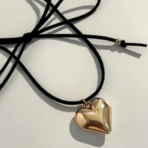 Macro shot of 3D gold heart pendant with black cord necklace and metallic accents