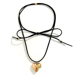 Detail of large gold heart pendant on adjustable black cord with bow and metallic beads