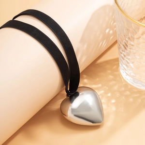 Detail of a shiny metallic heart pendant on a black grosgrain ribbon with water shadows