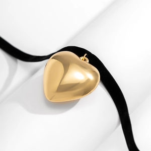 Macro detail of a large polished gold heart pendant on a black velvet choker necklace