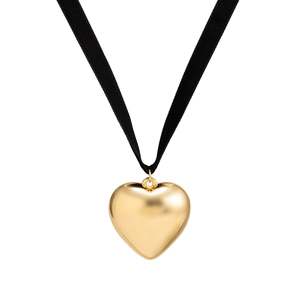 Detail view of bold gold heart pendant with black velvet ribbon strap on white background