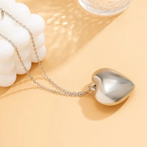Macro detail of high-polish silver heart pendant with fine link chain on a neutral base
