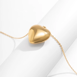 Macro shot of 3D polished golden heart pendant with a fine cable chain on white background