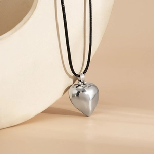Close-up of a polished silver heart pendant on a black cord over minimalist props