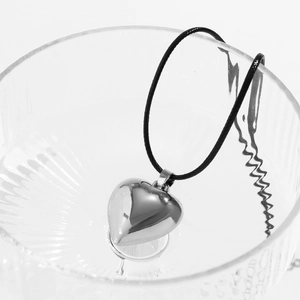Close-up of polished silver heart pendant with black cord on textured glass surface