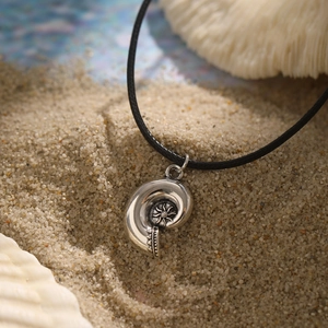 Detail of retro silver conch shell pendant with sun pattern on soft beach sand