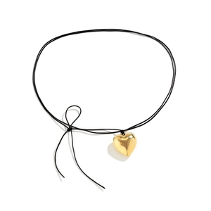 Detailopname van de gepolijste gouden hartvormige hanger met zwart koord en strik
