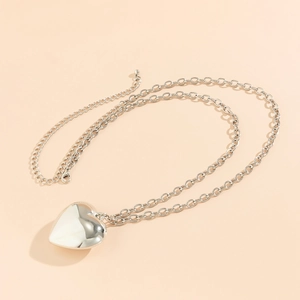 Detailopname van een grote zilveren hartvormige hanger aan een gepolijste metalen tailleketting