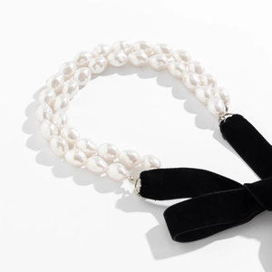 Detail van een dubbele barokke parelketting met een grote zwarte fluwelen strik