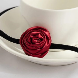 Macro shot of 3D red satin rose flower choker with black velvet straps on a coffee cup