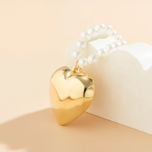 Gedetailleerde macro van een grote gepolijste gouden hart hanger met witte kralen