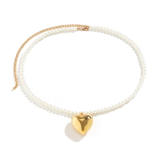 Detail van de grote gouden hartvormige hanger met glanzende afwerking en witte parelketting