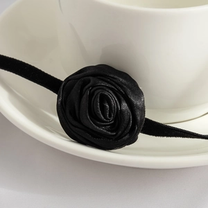 Close-up of a 3D black satin rose choker with velvet tie ribbons on white ceramic cup
