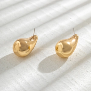 Detailed macro shot of high-polish gold teardrop earrings on a textured stone background