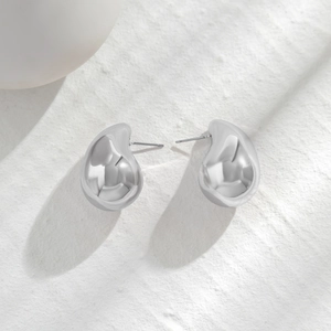 Detailed view of teardrop stud earrings with polished metallic finish on a textured background