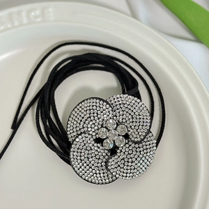 Detail van een haarelastiek met strass camelia bloem en zwarte koordjes voor dames