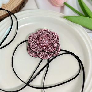 Detail macro-opname van de roze strass camelia bloem hanger aan een zwart lang koord