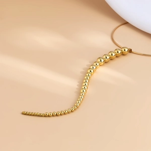 Detail der goldenen Choker-Halskette mit abgestuften Metallperlen auf warmem Grund