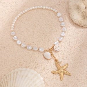 Macro shot of faux pearl necklace featuring gold starfish and white shell charms on sand