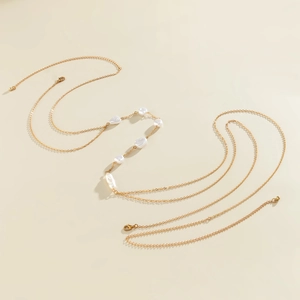 Close-up of gold finish body chain featuring irregular baroque pearls on a beige surface