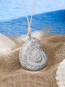 Macro detail of silver nautilus shell pendant on white cord over a sandy beach