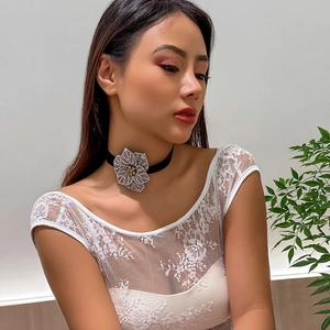 Detail of a black velvet choker featuring a large sparkling rhinestone flower on a model