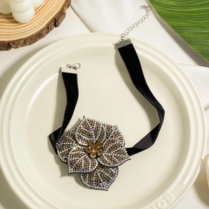 Detailed macro view of black velvet choker with rhinestone flower on white ceramic plate