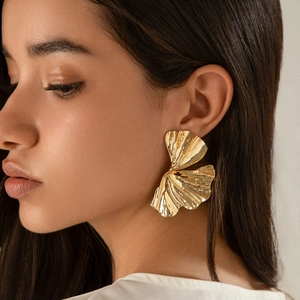 Primo piano di modella con grandi orecchini a foglia di ginkgo dorati con finitura ruvida