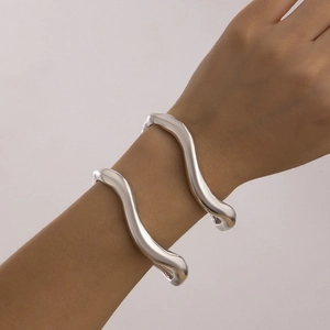 Detail van twee zilveren onregelmatige gegolfde armbanden met hoogglans afwerking