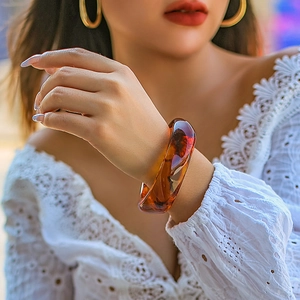 Close-up of a chunky amber translucent acrylic bangle on a model wearing white lace