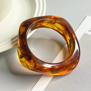 Macro detail of chunky amber acrylic resin bangle with artistic swirling brown patterns