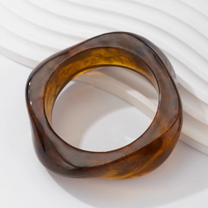Macro shot of irregular translucent amber resin bangle with artistic wave curve design
