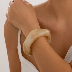 Detail of a creamy marble resin wide bangle with irregular wave design on a model wrist