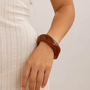 Detail of amber translucent irregular acrylic bangle worn on a white knit sleeve