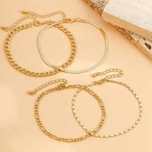 Detail view of four-piece gold anklet set with snake, ring, figaro, and beaded chains