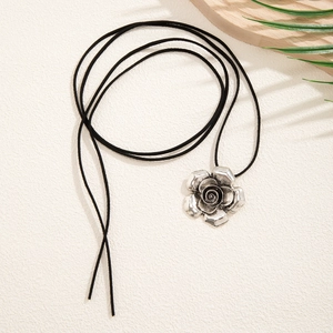 Dettaglio del ciondolo a rosa vintage in argento su cordino nero con sfondo rustico