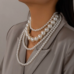 Detalle de collar de perlas multicapa con varios tamaños en modelo con traje gris