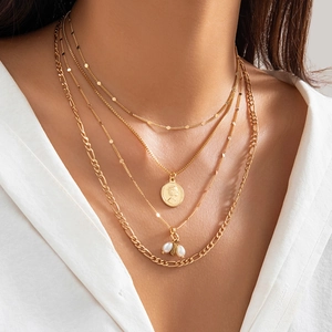 Detalle de collar dorado de varias capas con colgante de moneda y perlas en modelo