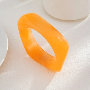 Detail of a bright orange translucent acrylic geometric bangle on white texture