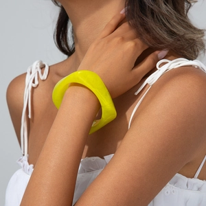 Detail of yellow translucent irregular resin bangle worn on wrist in a minimalist style