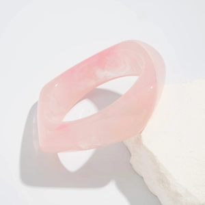 Detail view of pink irregular geometric acrylic bangle on a decorative white stone