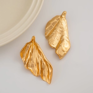 Dettaglio degli orecchini a foglia di ginkgo dorati con trama in metallo spazzolato e forma