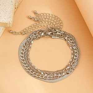 Detail of silver multilayer anklet set featuring snake, cable, and curb chain textures