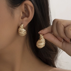 Detail of golden spiral shell earrings with textured finish on model and held by hand